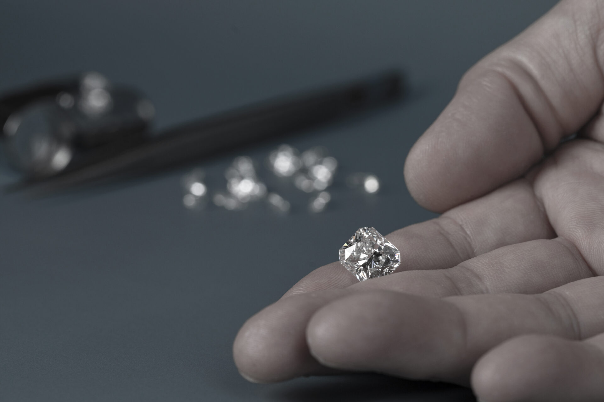Eine Hand, die einen großen, funkelnden Diamanten hält, mit mehreren kleineren Diamanten und einer Pinzette im Hintergrund auf einer blaugrauen Fläche, die den Wert und die Klarheit symbolisiert, die bei der Finanzierung von Bestattungen erforderlich sind.